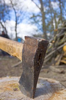 Close up shot of an axe in a stump with firewood in the background.