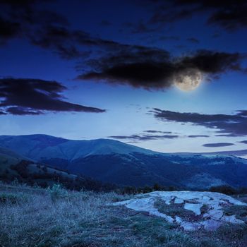 mountain landscape. valley with stones on the hillside. forest on the mountain under the beam of light falls on a clearing at the top of the hill. at night