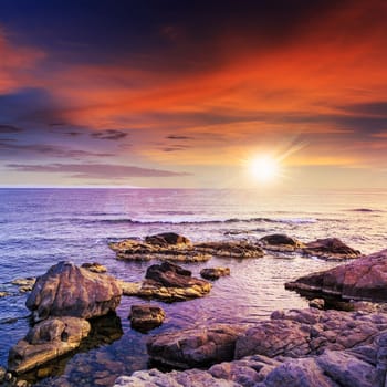 sea wave attacks the boulders and is broken about them at sunset