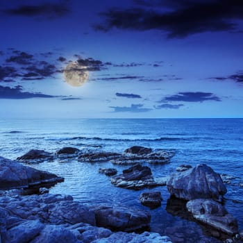 sea wave attacks the boulders and is broken about them at night in moon light