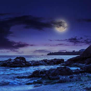 sea wave attacks the boulders and is broken about them at night in moon light