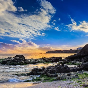 sea wave attacks the boulders and is broken about them at sunset