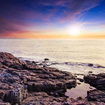 sea wave attacks the boulders and is broken about them at sunset