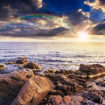 sea wave attacks the boulders and is broken about them at sunset with rainbow