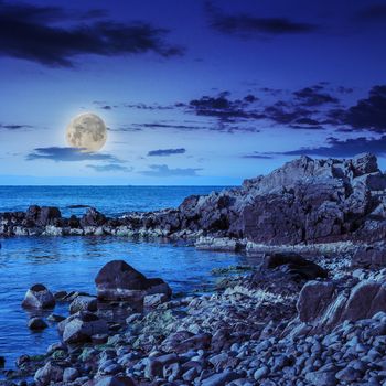 sea wave attacks the boulders and is broken about them at night in moon light