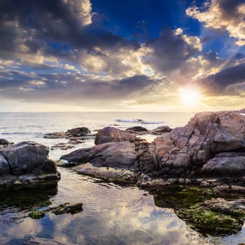 sea wave attacks the boulders and is broken about them at sunset