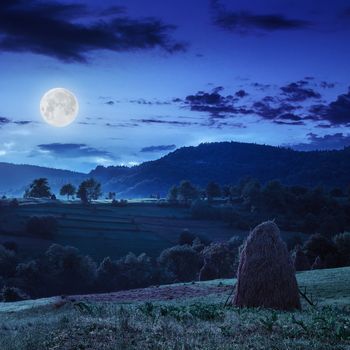 Stack of hay on a green meadow in the mountains in the morning under a blue summer sky at night in moon light