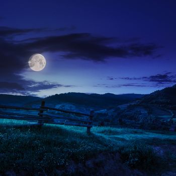 wooden fence in the grass on the hillside near the village at night in moon light