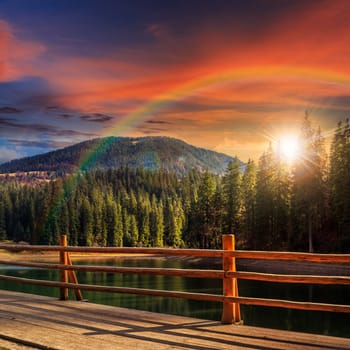 view from pier on lake near the pine forest on mountain background at sunset