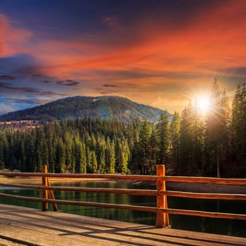 view from pier on lake near the pine forest on mountain background at sunset