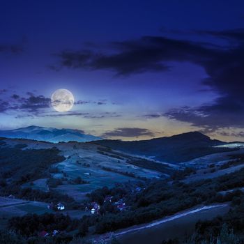 Stack of hay on a green meadow in the mountains under a blue summer sky at night in moon light