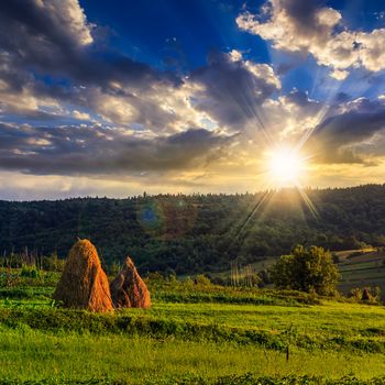 Stack of hay on a green meadow in the mountains under a cloudy summer sky at sunset