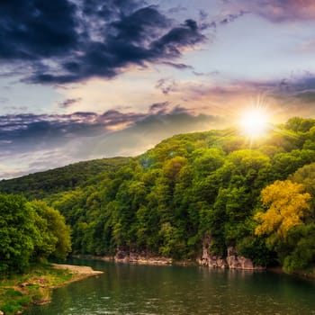 calm river flowing between green mountains on a cloudy summer sunset