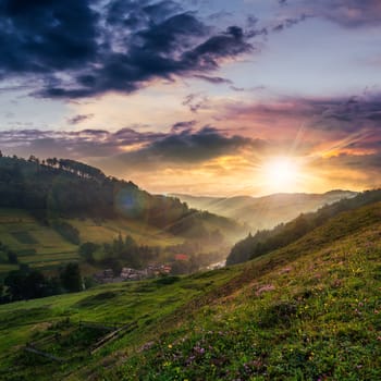 cold morning fog on a hillside meadow near mountain village at sunset