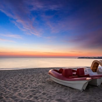 calm sea waves touch  sandy beach with few boats at sunrise