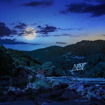 mountain river with stones and grass in the forest at the foon of mountain slope at night in moon light