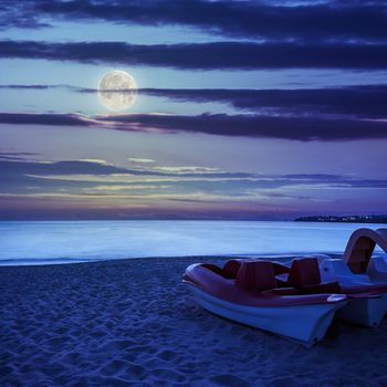 calm sea waves touch  sandy beach with few boats at night in moon light