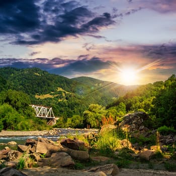 metall blidge over mountain river with stones and moss in the forest near the mountain slope at sunset