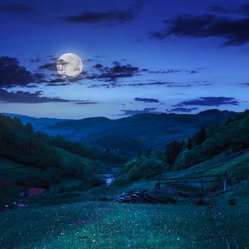 mountain summer landscape. trees and fence near meadow on hillside under  sky with clouds at night