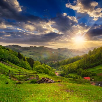 mountain summer landscape. trees and fence near meadow on hillside under  sky with clouds at sunset