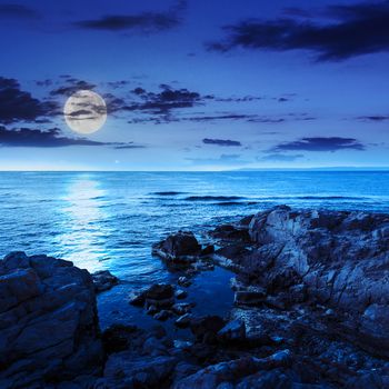calm sea with fiev waves on coast with  boulders and seaweed at night in moon light