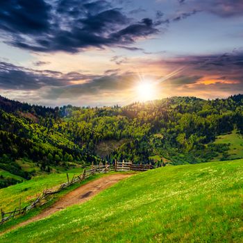 summer landscape. fence near the meadow path on the hillside. forest in fog on the mountain at sunset