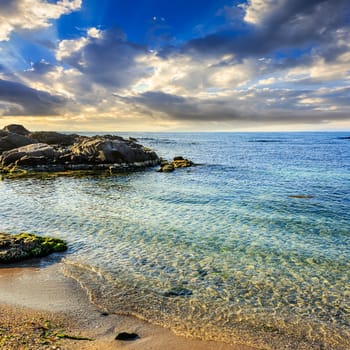 calm sea with some wave on  sandy beach with stones on sunrise