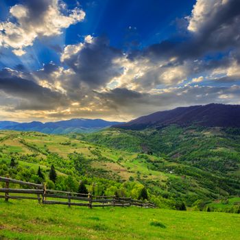 summer landscape. fence near the meadow on hillside. forest in fog on the mountain