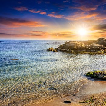 calm sea with some wave on  sandy beach with stones at sunset