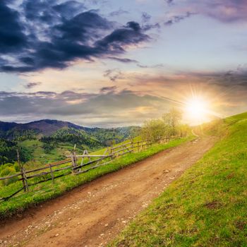 summer landscape. fence near the meadow path on the hillside. forest in fog on the mountain at sunset