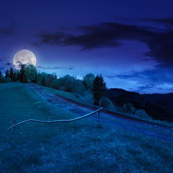 summer landscape. fence near the meadow path going up on the hillside. forest in fog on the mountain at night in moon light