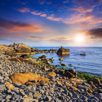 sea wave attacks the boulders and is broken about them at sunset