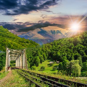 old railroad passes through the metal bridge in the mountain village at sunset