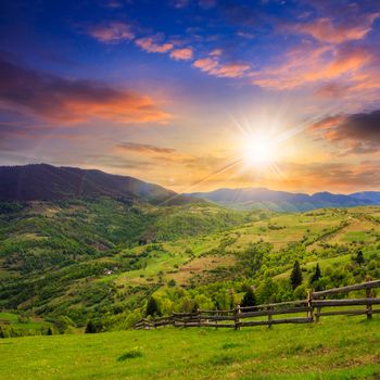 summer landscape. fence near the meadow on hillside. forest in fog on the mountain at sunset