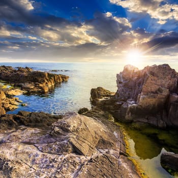 calm sea wave touch giant boulders on rocky shore at sunset