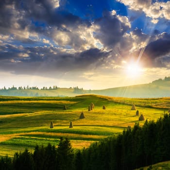 Stack of hay on a green meadow in the mountains at sunset under a blue summer sky