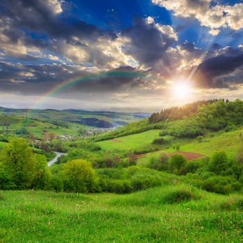 summer landscape. village on the hillside. forest on the mountain light fall on clearing on mountains at sunset with rainbow