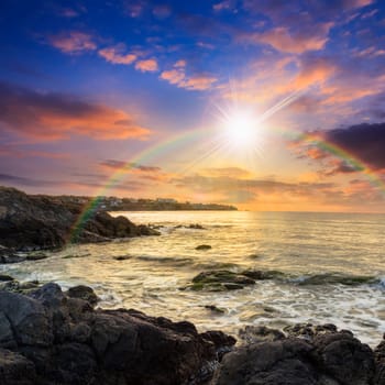 sea wave attacks the boulders and is broken about them at sunset with rainbow