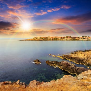 ancient european city on a rocky shore near sea in summer at sunset with rainbow