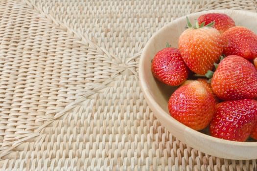 fresh strawberry in wooden bowl on wickerwork background