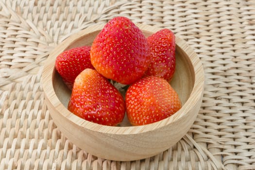 fresh strawberry in wooden bowl on wickerwork background