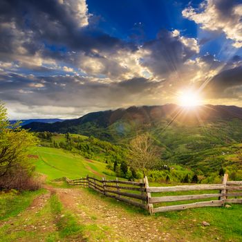 summer landscape. fence near the meadow path on the hillside. forest in fog on the mountai at sunset