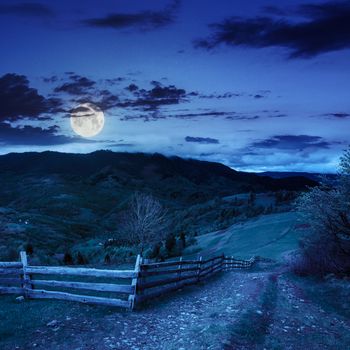 summer landscape. fence near the meadow path on the hillside. forest in fog on the mountain at night in moon light