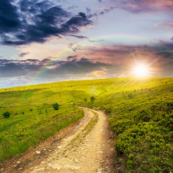 gravel road going on hillside to highlands at sunset with rainbow