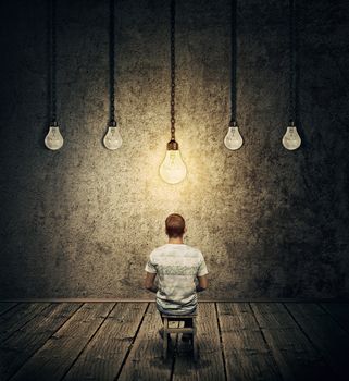 Creative idea concept with a person sitting in a dark room with suspended lightbulbs and one glowing over head. Symbolizing smart person having idea