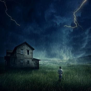 Spooky landscape as a young boy walking in the meadow look at a ghost, haunted house below a dark stormy sky. 