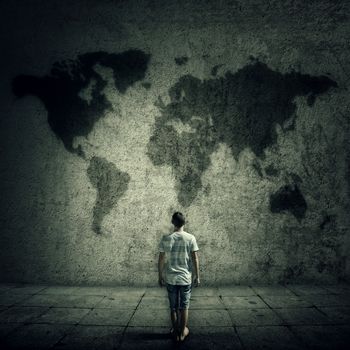 Man surrounded by limitations, daily routine, looking at the world map on a concrete wall. International travel cocept.