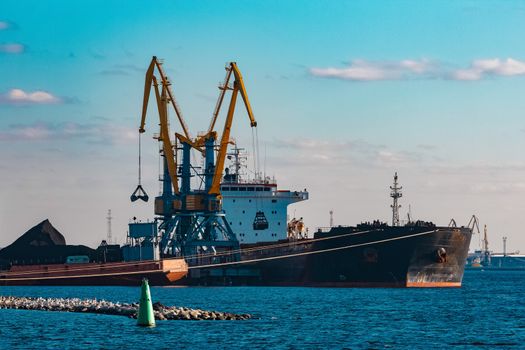 Black cargo ship loading with a coal at the port