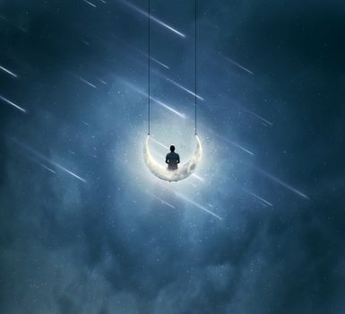 Surreal background with a boy sitting on a crescent moon, as a swing, over a misty night sky