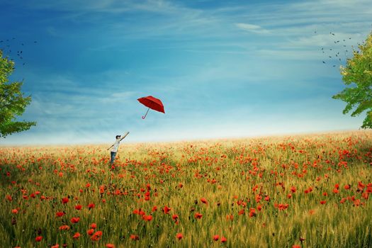 Young boy stand on a country meadow with million of red poppies, trying to catch his red umbrella that fly to the sky. The pursuit of happiness and success concept. Life joy, fun and happiness.